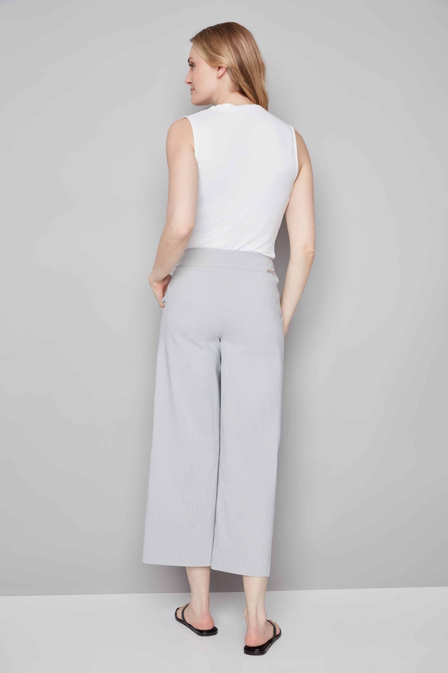 Woman wearing a white sleeveless top and gray wide-leg pants on a plain background