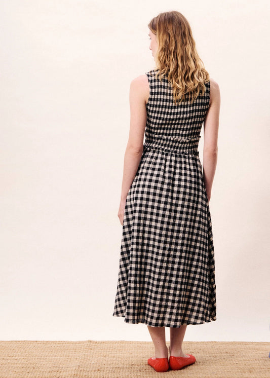 Woman in a black and white checkered dress standing next to a blue vase with a white background