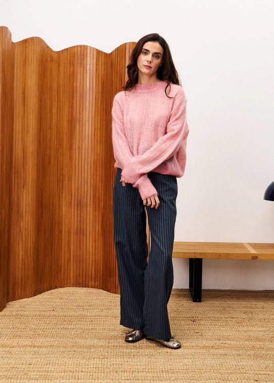 Woman wearing a pink sweater and dark pants standing in a room with wooden paneling. FRNCH Lys Sweater | Pale Pink, Designed in France