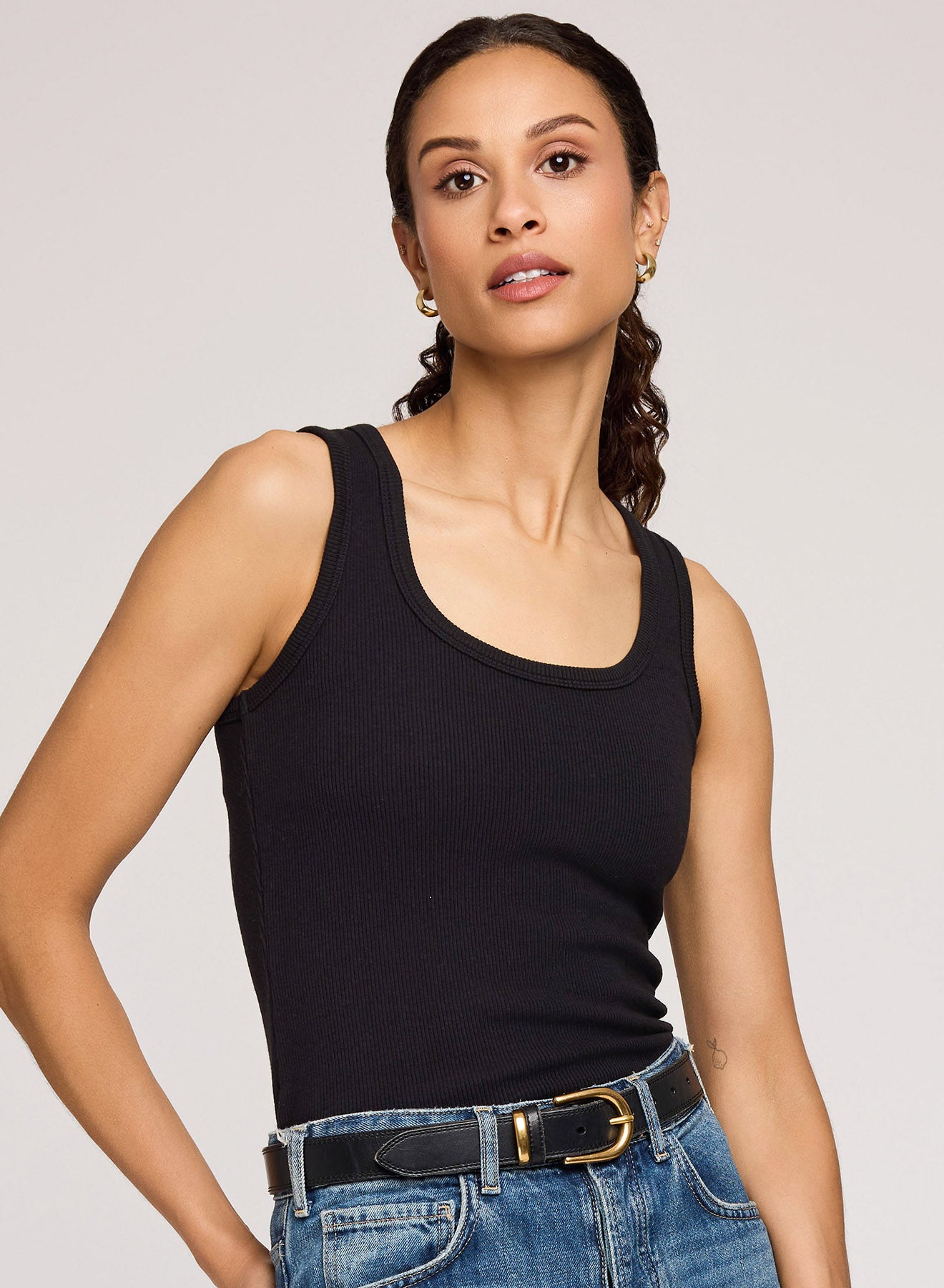 Woman wearing a black tank top and blue jeans against a plain background
