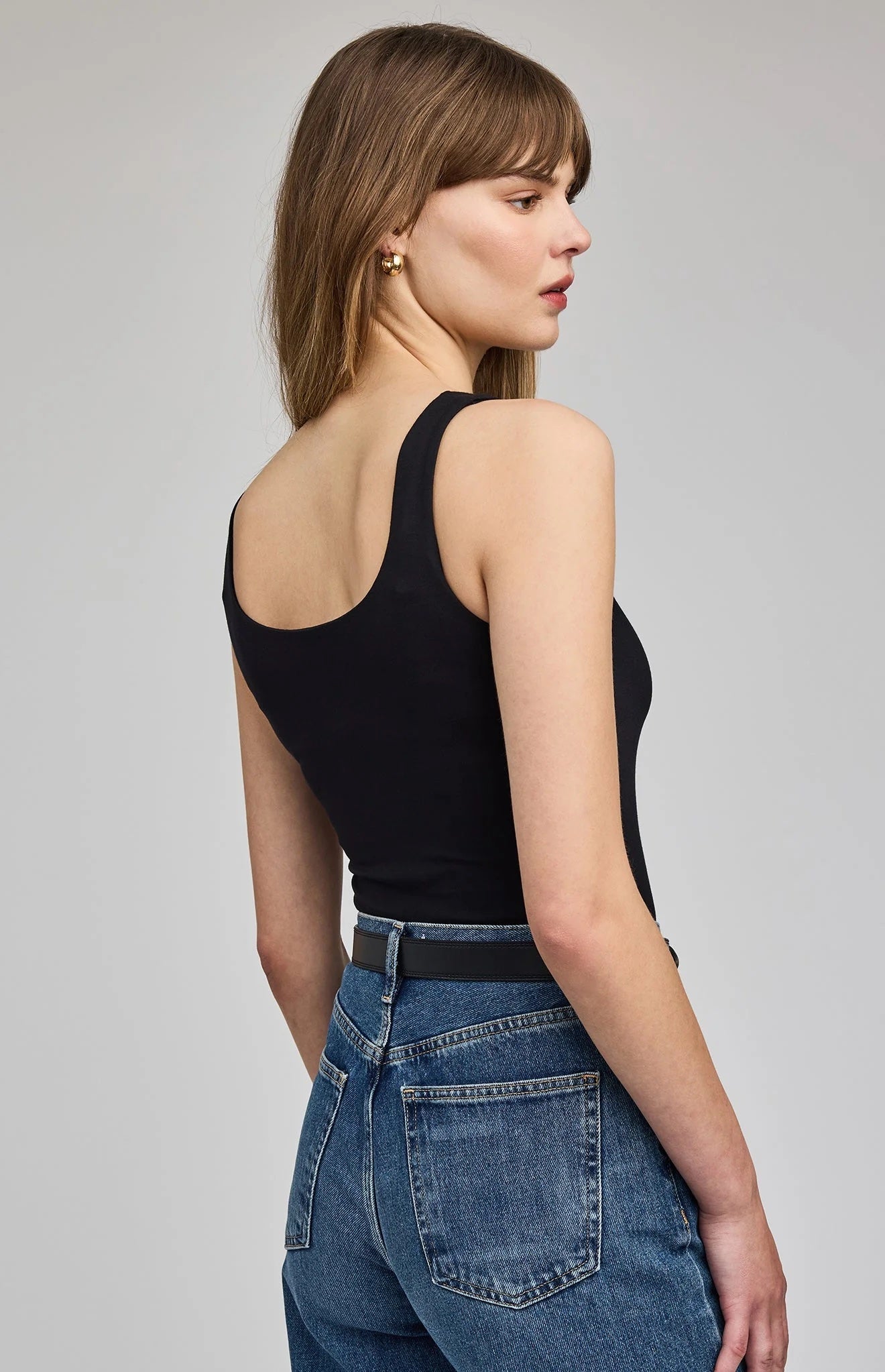 Woman wearing a black tank top and blue jeans on a gray background