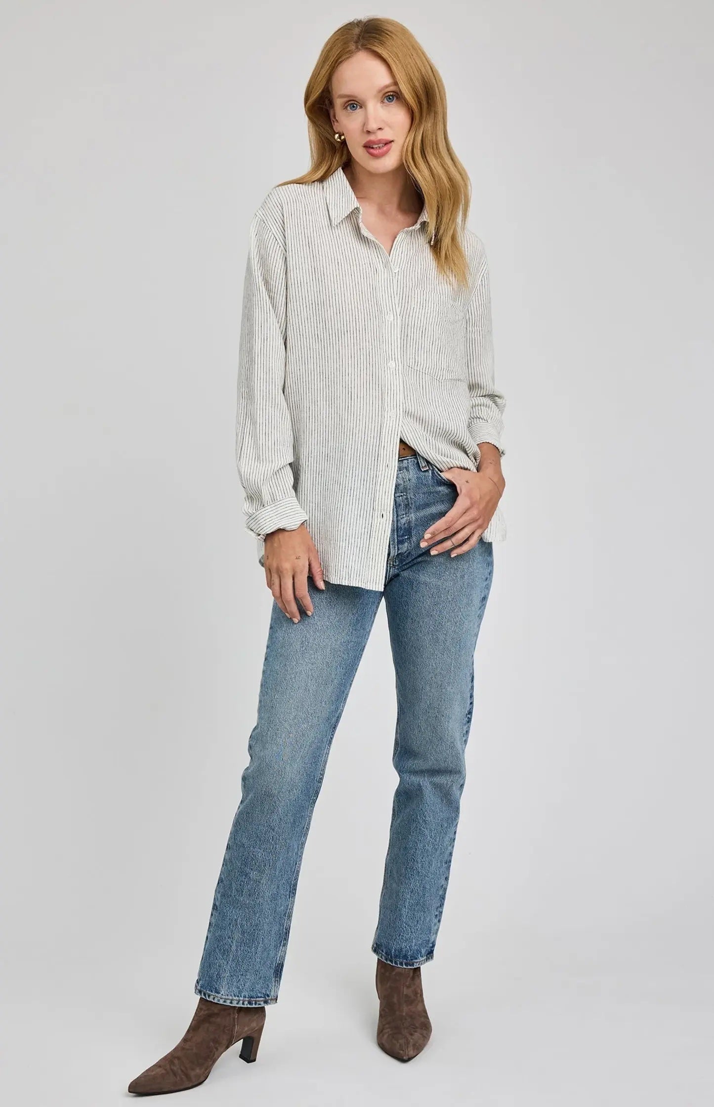 Woman wearing a light-colored shirt and blue jeans on a white background