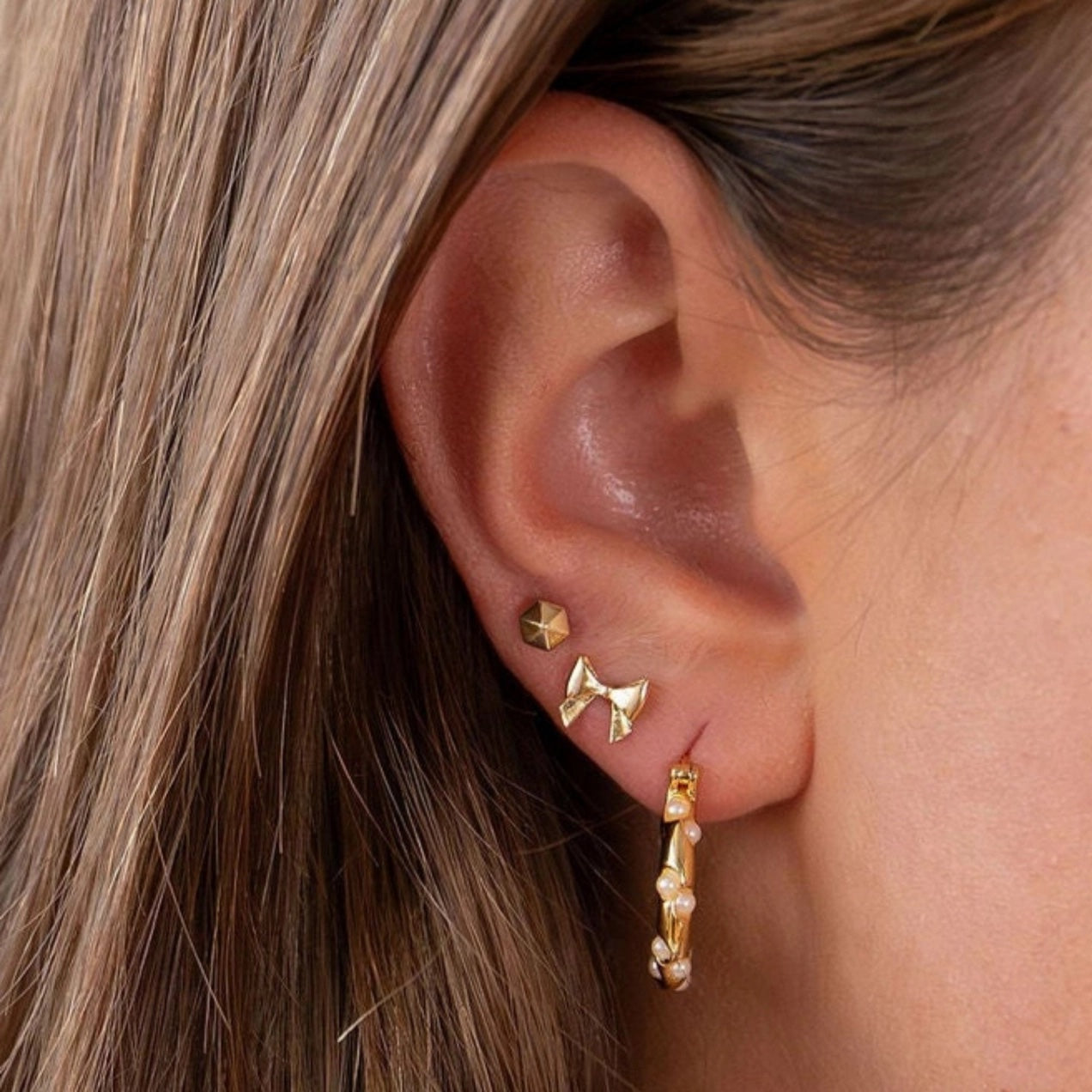 Close-up of an ear wearing gold earrings with a blurred background