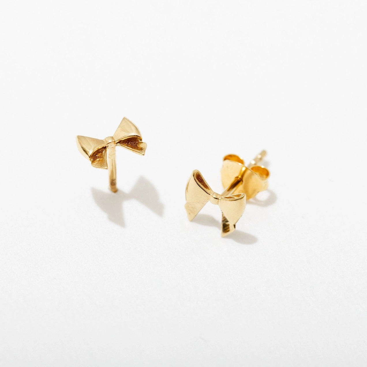 Gold bow-shaped earrings on a light gray background