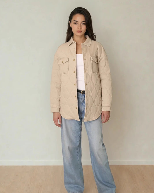 Woman wearing a beige quilted jacket and light blue jeans against a plain background