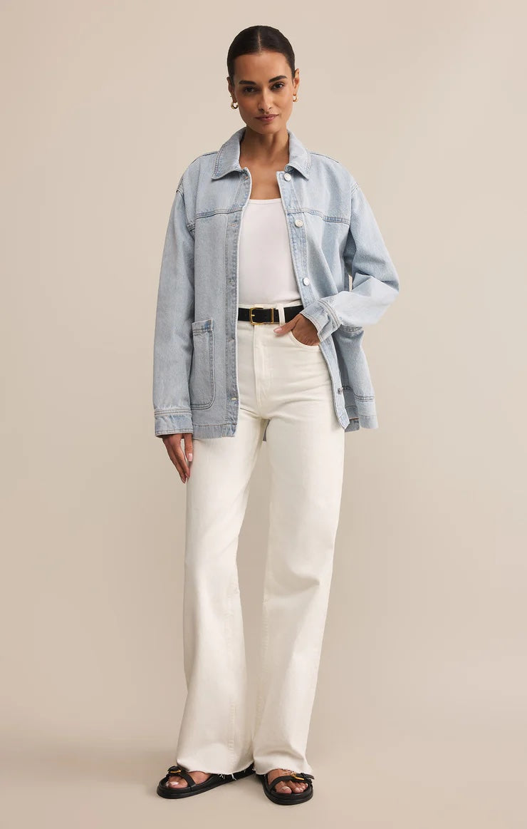 Woman wearing a light blue denim jacket, white top, and white pants on a beige background