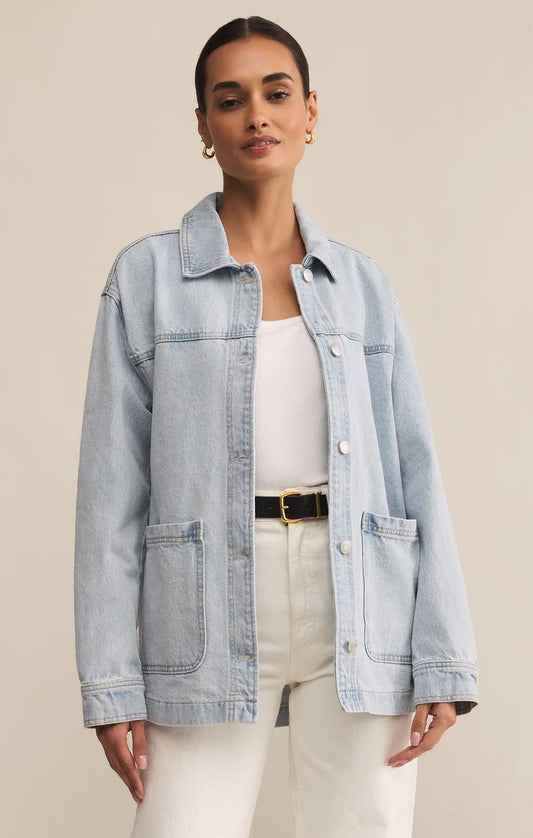 Woman wearing a light blue denim jacket over a white top on a beige background | Z Supply On The Road Denim Jacket | Faded Indigo, Designed in USA