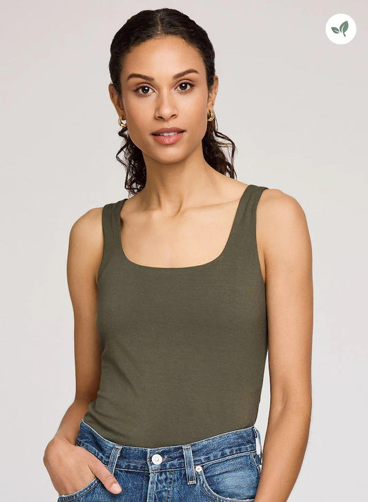 Woman wearing an olive green tank top and blue jeans on a plain background