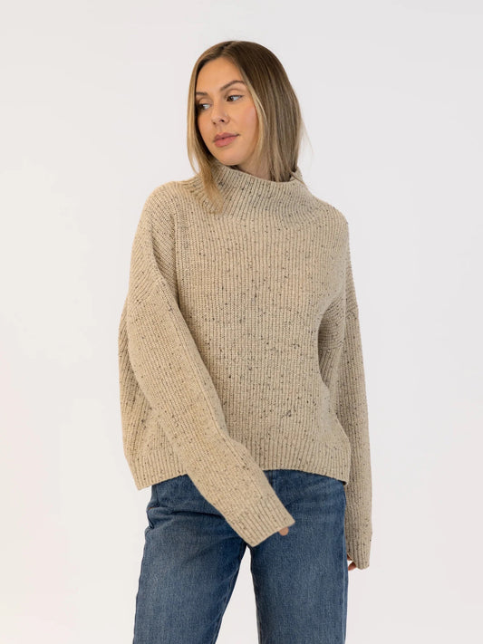 Woman wearing a beige knitted sweater and blue jeans on a white background | Lyla + Luxe Evolet Fleck Sweater | Neutral