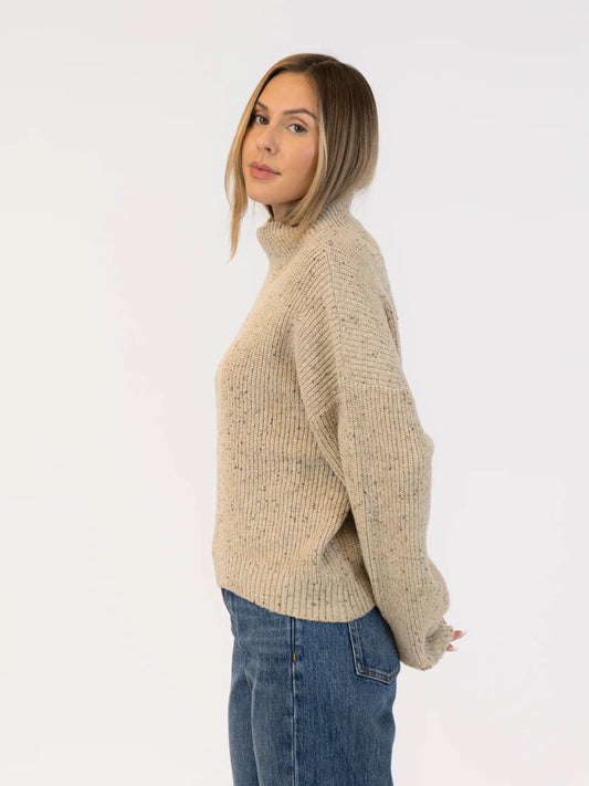 Woman wearing a beige knitted sweater and blue jeans on a white background | Lyla + Luxe Evolet Fleck Sweater | Neutral