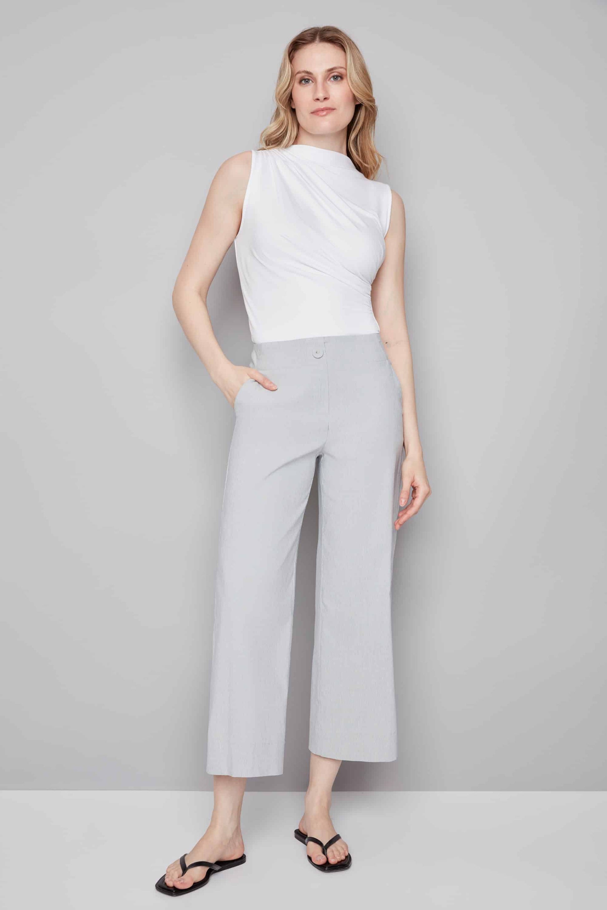 Woman wearing a white sleeveless top and light gray wide-leg pants against a plain background