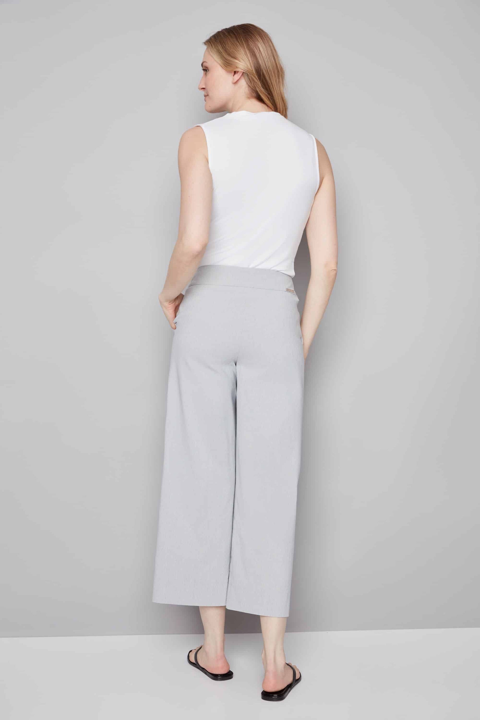 Woman wearing a white sleeveless top and gray wide-leg pants on a plain background