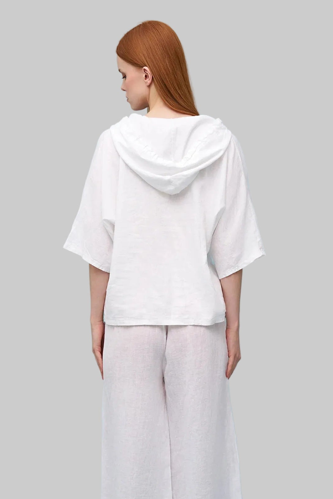 Woman wearing a white top and light gray pants against a light grey background