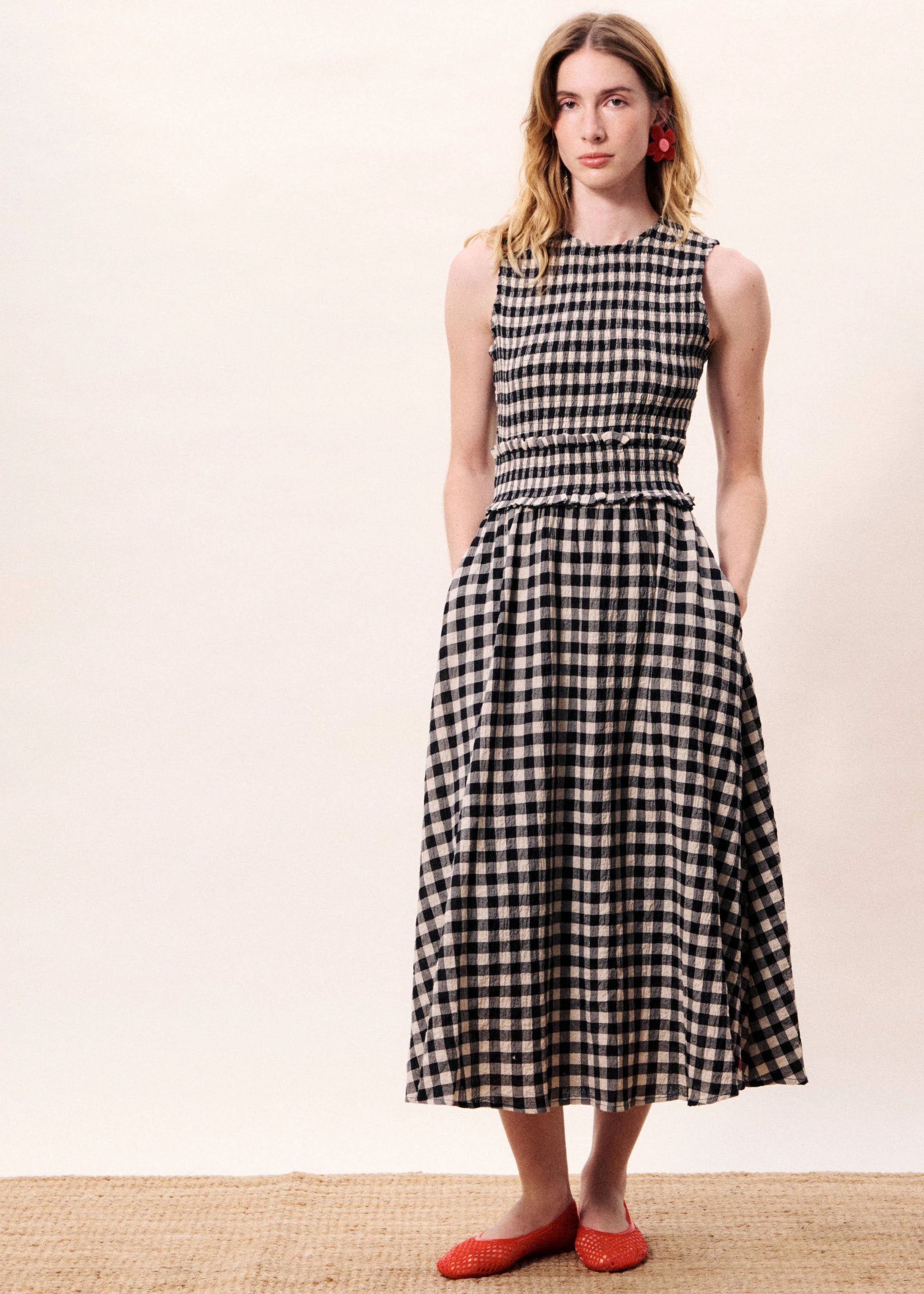 Woman wearing a black and white checkered dress standing next to a blue decorative vase on a beige background