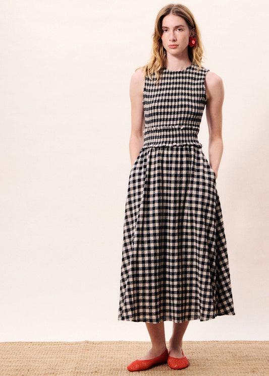 Woman wearing a black and white checkered dress standing next to a blue decorative vase on a beige background