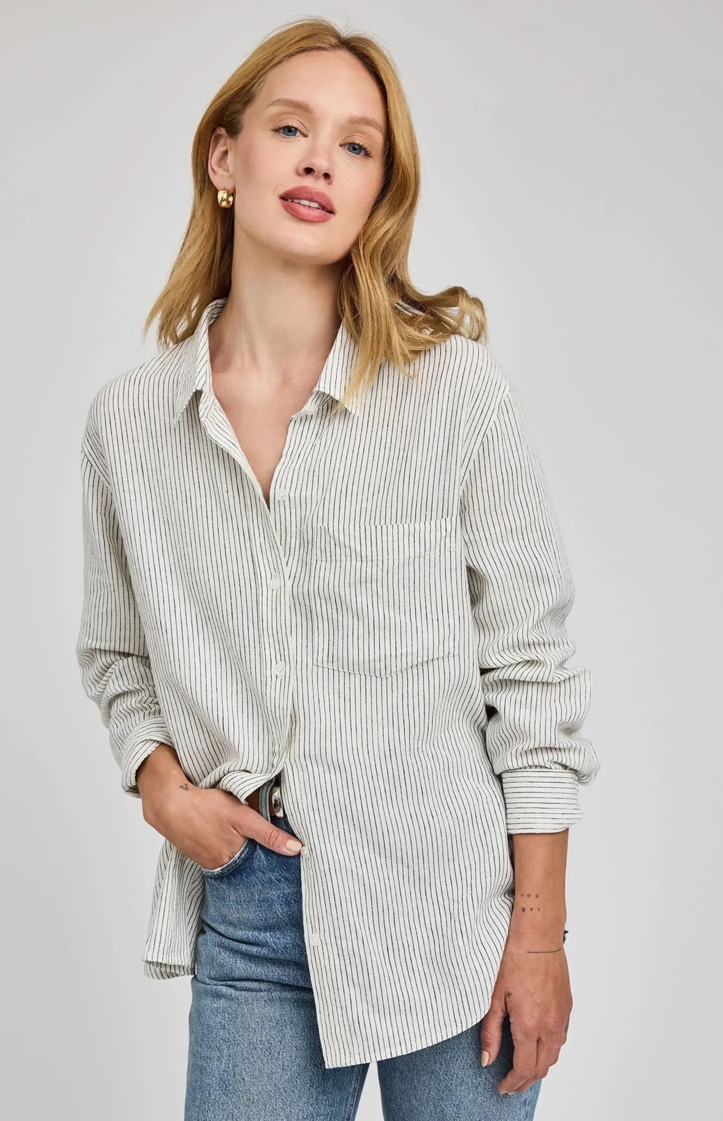 Woman wearing a striped shirt over a collared shirt with blue jeans on a plain background