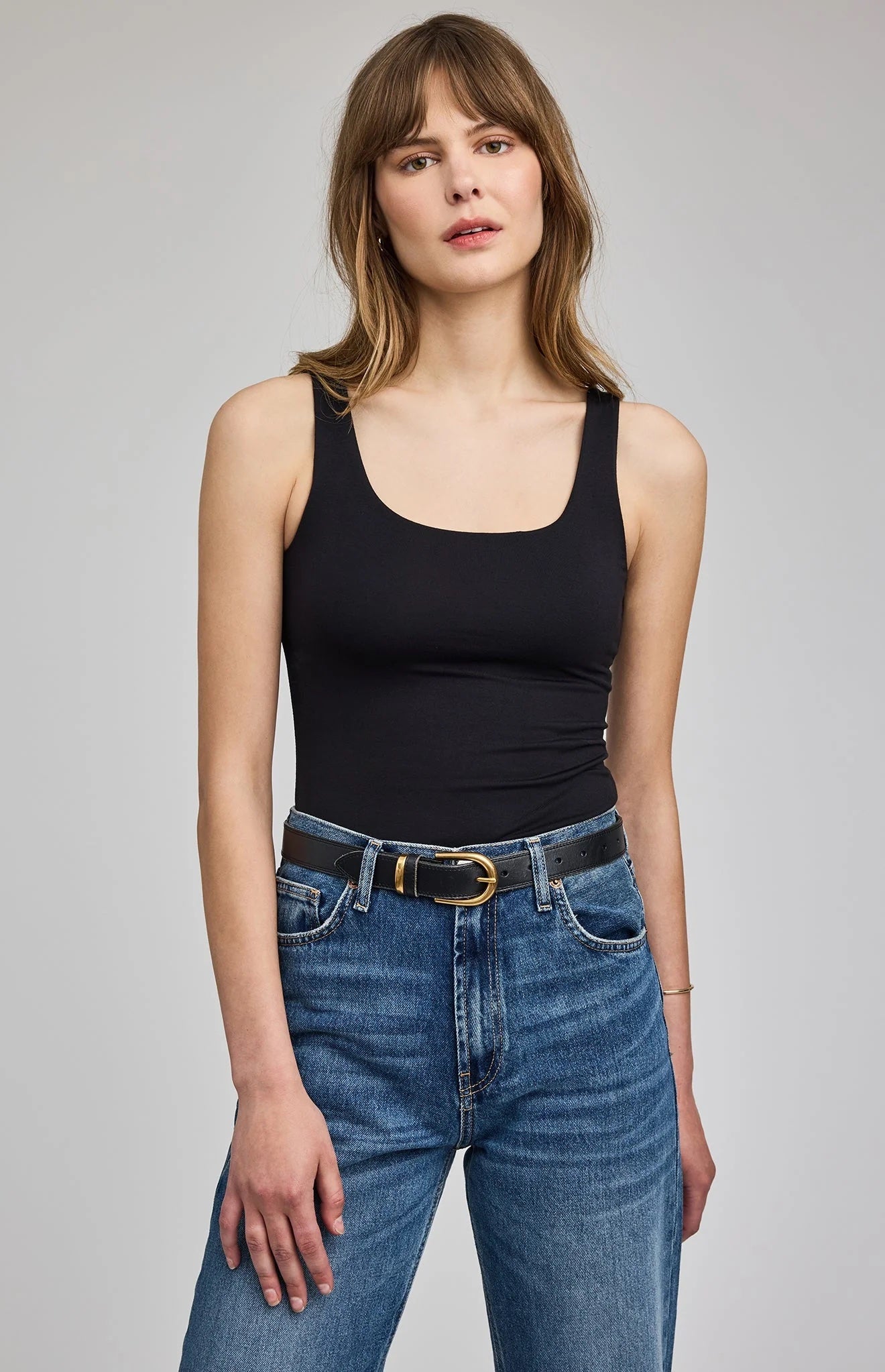Woman wearing a black tank top and blue jeans on a gray background