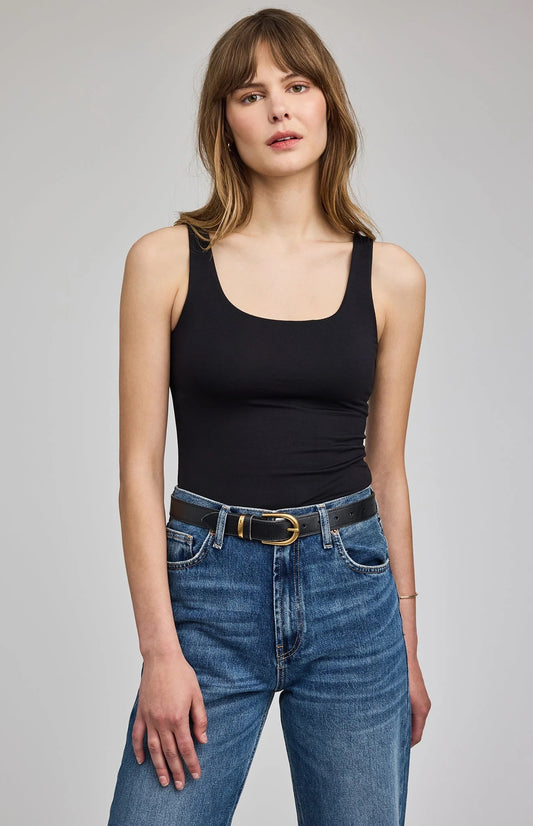 Woman wearing a black tank top and blue jeans on a gray background