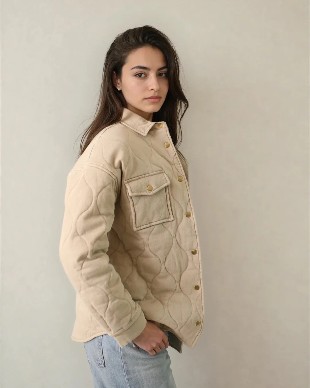 Woman wearing a beige quilted jacket against a plain background