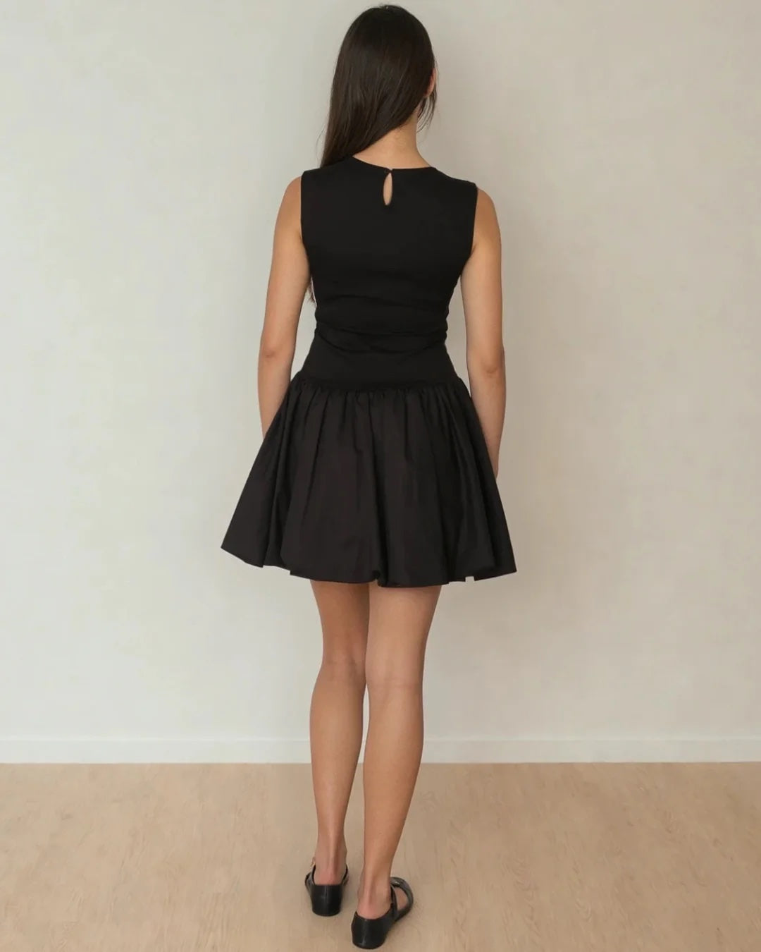 Person wearing a black dress standing against a plain background