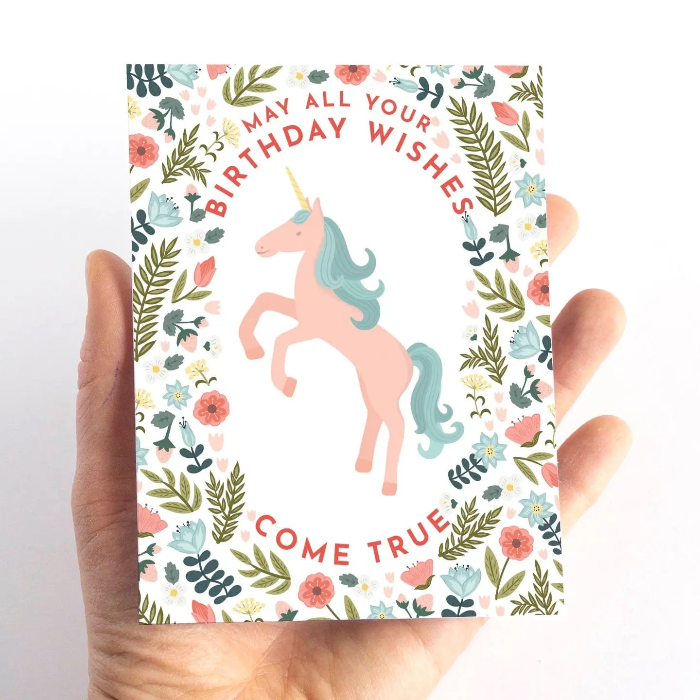Hand holding a card with a unicorn design and floral elements on a white background