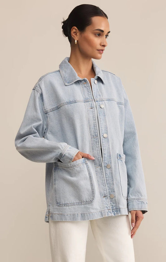 Woman wearing a light blue denim jacket against a beige background