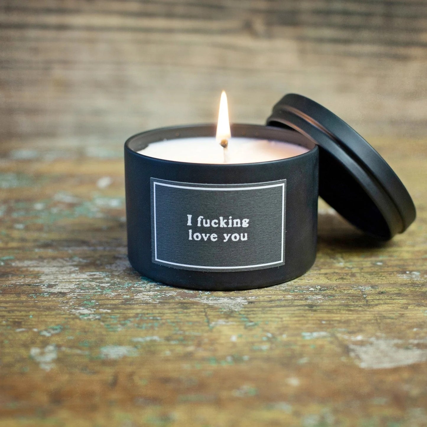 Candle in a black container with 'I fucking love you' text on a wooden surface