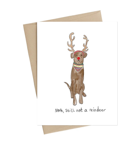 Card with a dog wearing reindeer antlers and a red nose, with text 'Note, still not a reindeer', on a white background | Little May Papery Holiday Card Not a Reindeer | Printed in Canada