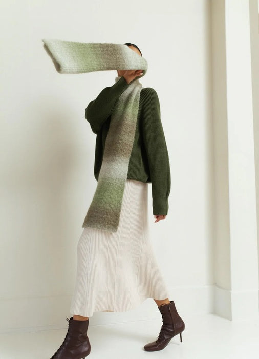 Person wearing a green sweater and white pants with a matching green scarf against a white background