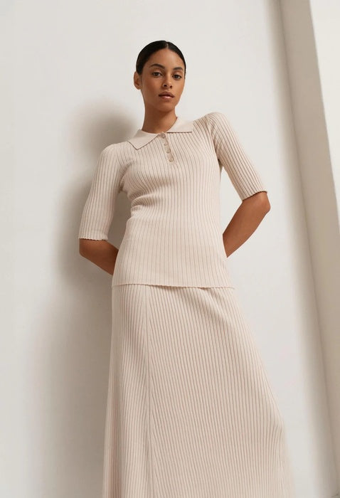 Woman wearing a beige ribbed dress against a plain background