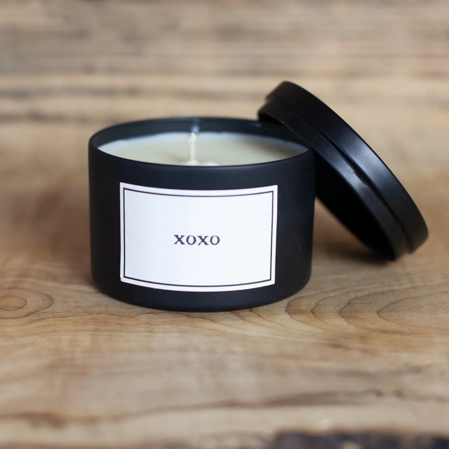 Black candle with a 'XOXO' label on a wooden surface