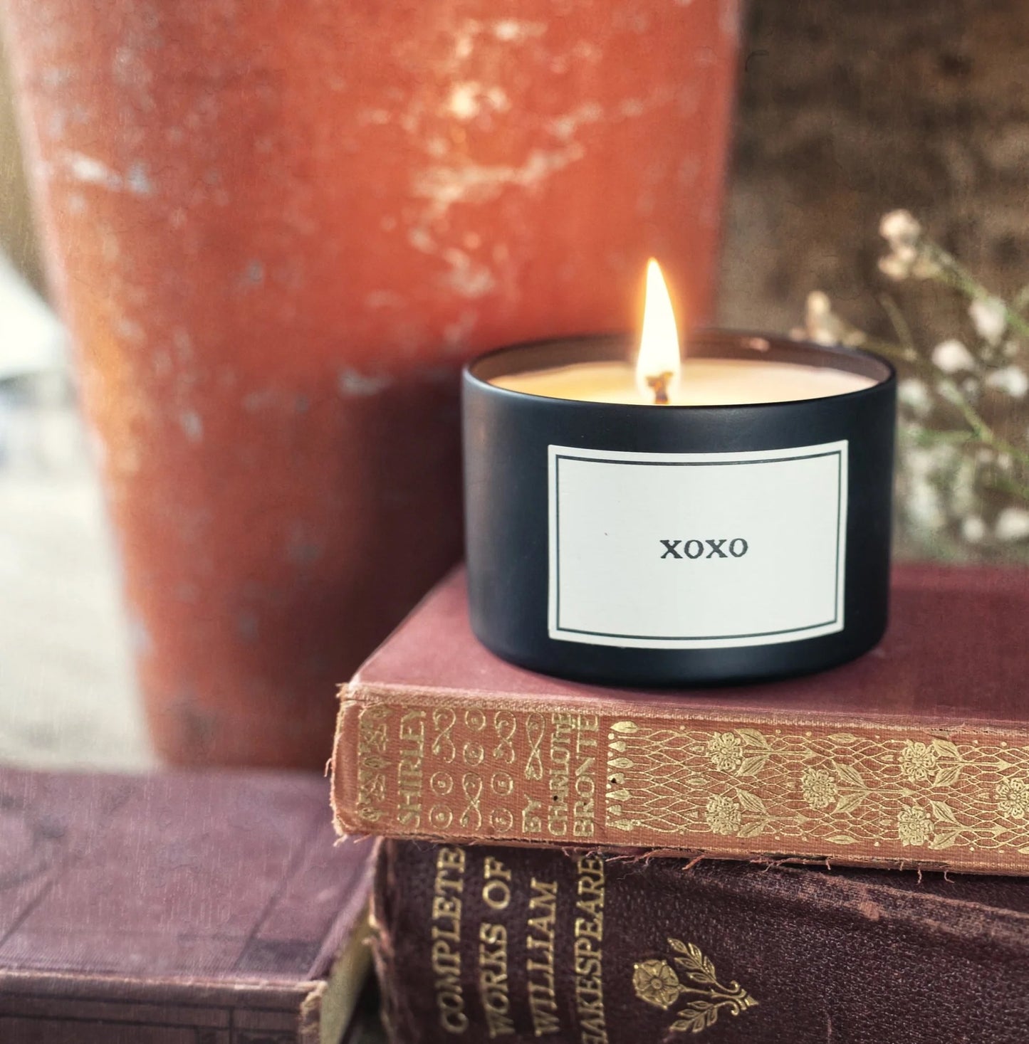 Candle labeled 'xoxo' on top of vintage books with a blurred background