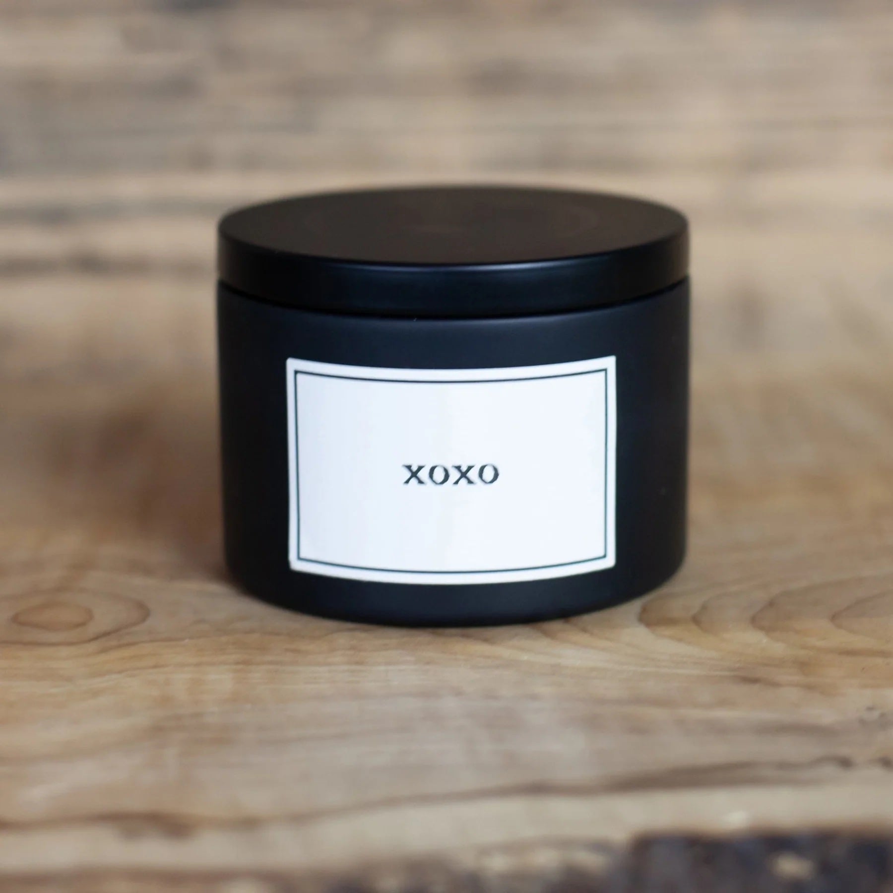 Black candle jar with 'XOXO' label on a wooden surface
